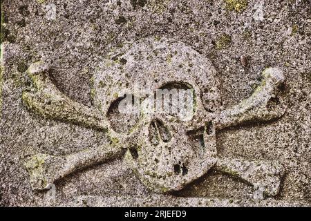 Sculptured skull and crossbones, an old mortality symbol, on a medieval, weathered and lichen-covered tombstone. Stock Photo