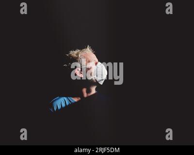 Side view of male shaper in protective respiratory mask standing in dark room near window with closed eyes Stock Photo