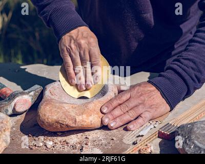 From above of crop anonymous male artisan grinding rock with sandpaper while making stone craft in open air workshop Stock Photo