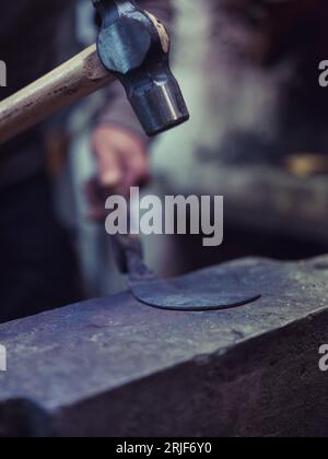 Closeup of crop anonymous blacksmith using hammer while forging metal on old anvil in traditional workshop Stock Photo