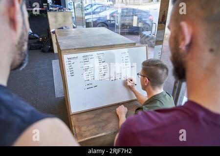 Back view of crop unrecognizable male workers writing notes on whiteboard while working together in light workspace Stock Photo