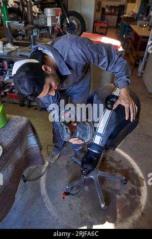 Full body of professional male mechanic in workwear polishing motorcycle fuel tank with grinding machine while working in garage Stock Photo