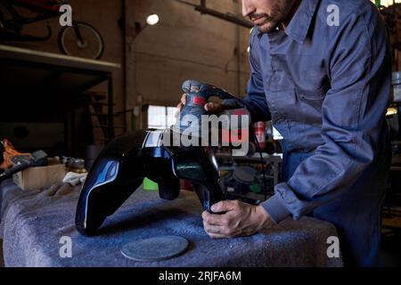 Crop anonymous concentrate male mechanic in workwear using angular grinding machine while working in dark garage Stock Photo