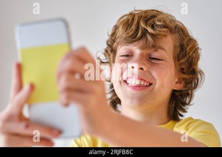 Smiling kid with freckled face skin and brown hair taking self portrait on mobile phone Stock Photo