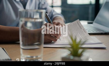 Close up male hands writing exam in class business paperwork with glass of water on office desk unrecognizable man businessman student studying write Stock Photo