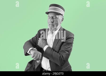 The train conductor looks at his wristwatch. Portrait of a train controller on a green background. Art black and white Stock Photo
