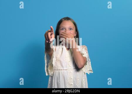 a girl in an old dress is scared of something. portrait on a blue background Stock Photo