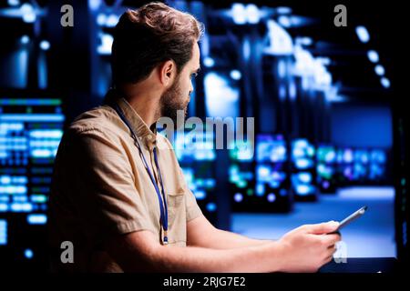 Qualified computer scientist resolving performance related issues in server rows. Programmer utilizing tablet to identify operational problems causing high tech establishment hardware slowdown Stock Photo