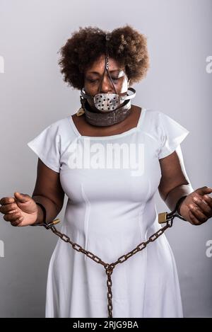 Portrait of a black woman in chains with an iron mask over her mouth. Slavery in Brazil. Arms in prayer. Studio reproduction. Stock Photo