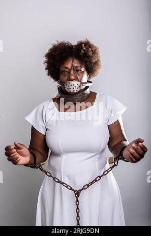 Portrait of a black woman in chains with an iron mask over her mouth. Slavery in Brazil. Arms in prayer. Studio reproduction. Stock Photo