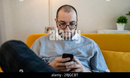 Cheerful young businessman using phone at home. Man working on smartphone via internet. Modern lifestyle and online work concept. Stock Photo