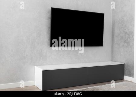 Part of the interior of a modern living room, a smart LED TV on a gray wall, a gray cabinet, a carpet. Minimalism in the interior. Stock Photo