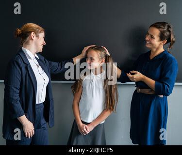 The teacher praises the schoolgirl in front of her mother standing at the blackboard.  Stock Photo