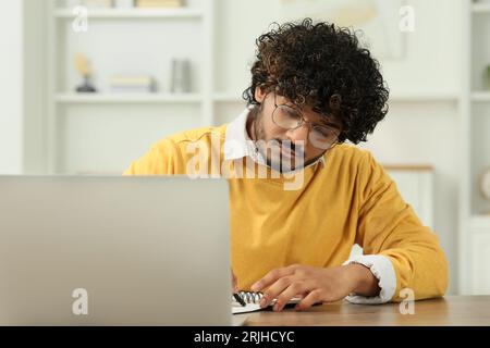 Handsome man taking notes near laptop in room Stock Photo