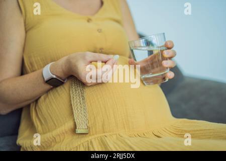 Prenatal Vitamins. Portrait Of Beautiful Smiling Pregnant Woman Holding Supplement and a glass of water, Taking Supplements For Healthy Pregnancy Stock Photo