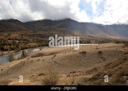 View from the top of the hill to the turn of a beautiful river flowing through the steppe, bending around a high mountain overgrown with coniferous fo Stock Photo