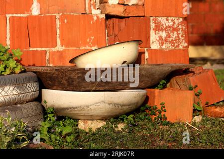 Bunch of old junk in suburban family house backyard next to red building blocks wall consisting of old white partially rusted metallic washbowl on top Stock Photo