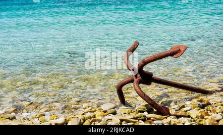 Closeup of an old grapnel anchor lying abandoned and rusting, on the water's edge of a pebbled beach in the Falkland Islands. Stock Photo