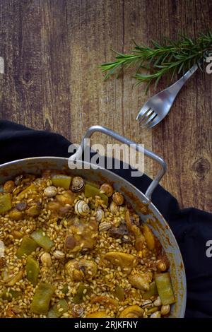 paella valenciana on cloth, with a fork and a sprig of rosemary on a wooden table, vertical. Stock Photo