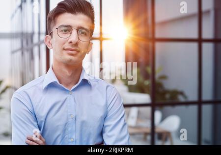 Confident sincere young businessman stands in the office with his hands crossed Stock Photo