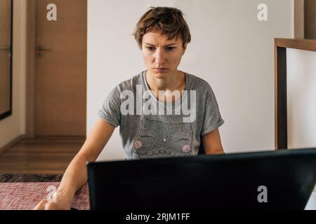 A woman in home clothes works at home at laptops with a tense look. Stock Photo