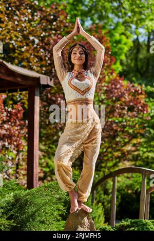joyful indian woman in elegant ethnic wear standing with raised praying hands, summer happiness Stock Photo