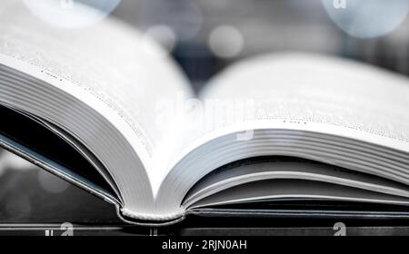 Open illuminated book on wooden table with glitters. Book lying open on desk in library. Glowing pages. Stock Photo