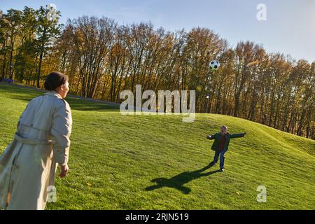 amazed african american boy playing football with mother on green field, screaming, running, soccer Stock Photo