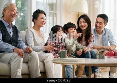 multi generational asian family sitting on couch in living room watching televesion happy and smiling Stock Photo