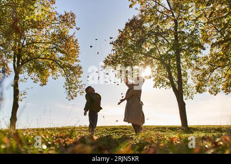 silhouette of mother and child throwing autumn leaves, park, fall season, having fun, freedom Stock Photo