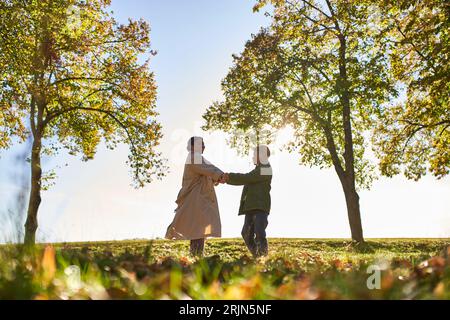 silhouette of woman and boy holding hands in autumn park, fall, bonding between mother and son Stock Photo