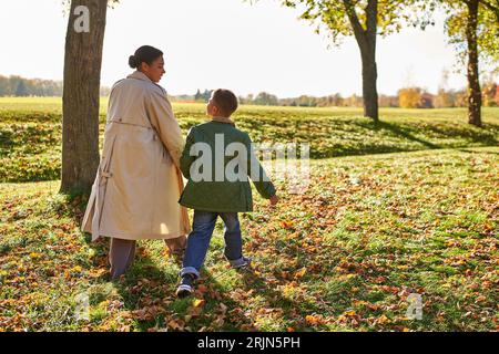golden hour, mother and son walking in park, autumn leaves, fall season, african american family Stock Photo