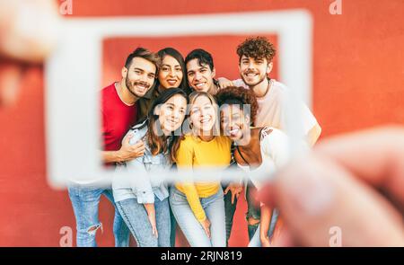 Happy multiracial friends taking a photo with istant camera paper style - Young people having fun using vintage photography trends - Main focus on fac Stock Photo