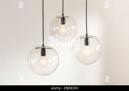 Three glass pendant lights suspended from the ceiling, each featuring a light bulb atop a frosted glass shade Stock Photo