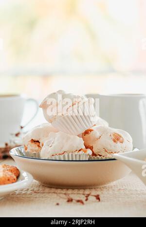closeup of a white ceramic bowl with some spanish merengues almendrados, baked meringues with almonds, placed on a table next to some ceramic bowls an Stock Photo