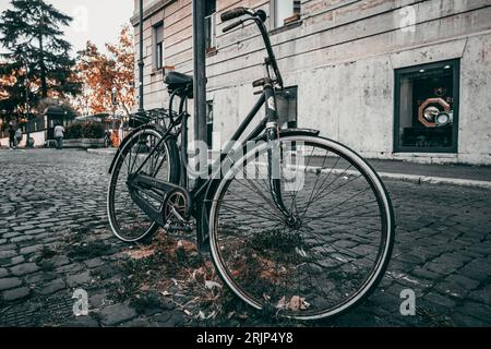 A black bicycle is parked against a street post on a cobblestone street. Stock Photo