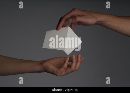Photography of a hand giving a paper to other had with gray background Stock Photo