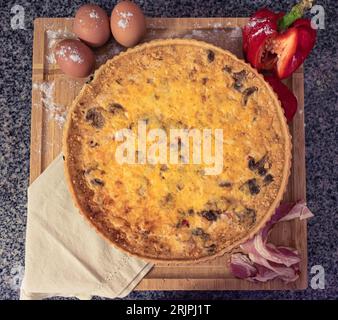 A Quiche based on chicken, peppers, eggs, mushrooms, chees, and bacon. On a wooden base and decorated with a neutral-colored napkin Stock Photo
