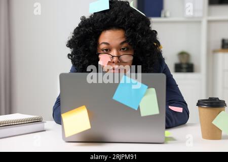Deadline concept. Tired woman working with laptop in office. Many sticky notes everywhere as reminders Stock Photo
