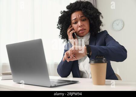 Deadline concept. Scared woman talking on smartphone and checking time in office Stock Photo