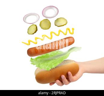 Woman making hot dog on white background, closeup. Ingredients levitating over bun Stock Photo