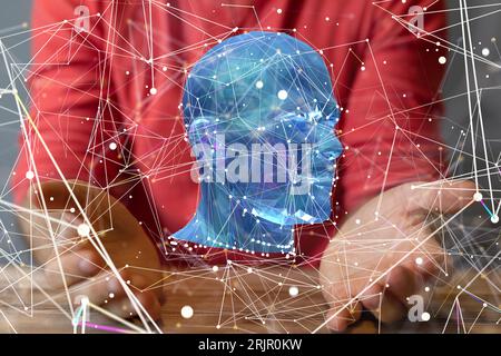 A man in a red shirt holding his hands under a blue hologram of a head Stock Photo