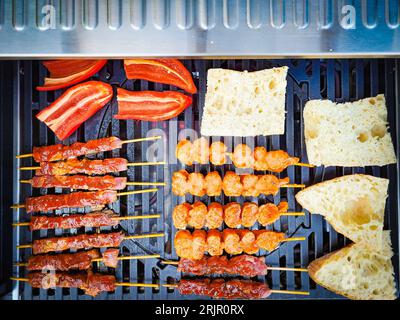 An overhead view of a grill with raw meat, bread pieces and red peppers placed on it Stock Photo
