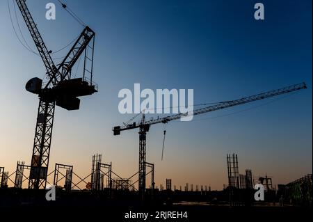 Silhouettes of two tower cranes on the construction site Stock Photo