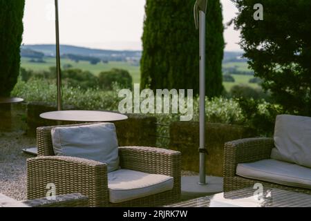 A patio with wicker furniture, including a sofa, chairs, and a coffee table, beneath a large window that affords a view of the outdoors Stock Photo