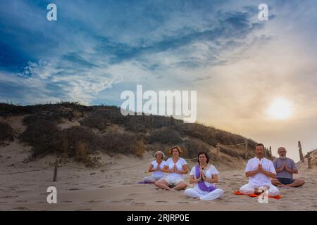 Group of men and women practicing yoga on the sand at the beach. Padmasana or lotus asana Stock Photo