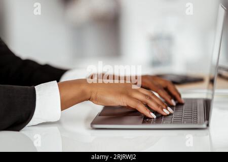Closeup of black businesswoman using laptop, typing on keyboard, writing email, sitting in office, selective focus Stock Photo