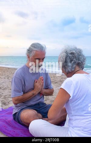 Couple meditating together in a prayer sitting position favoring the personal relationship on the beach Stock Photo