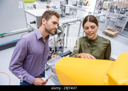 Businessman and woman having a meeting in front of industrial robots in a high tech company Stock Photo
