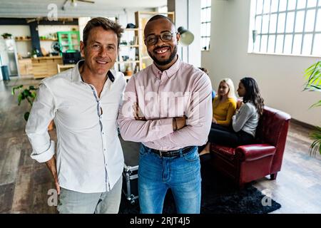 Portrait of two smiling businessmen with coworkers in background in loft office Stock Photo